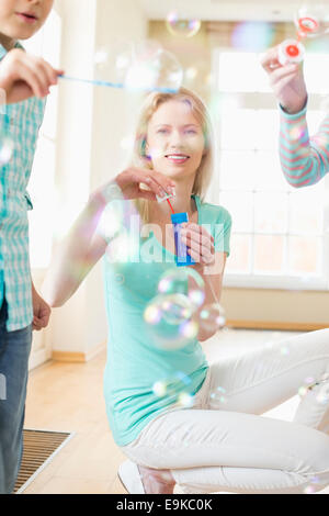 Felice madre e bambini che giocano con bacchette di bolle a casa Foto Stock