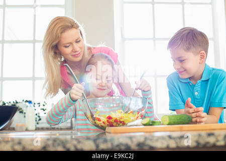 Famiglia guardando ragazza insalata di miscelazione in cucina Foto Stock