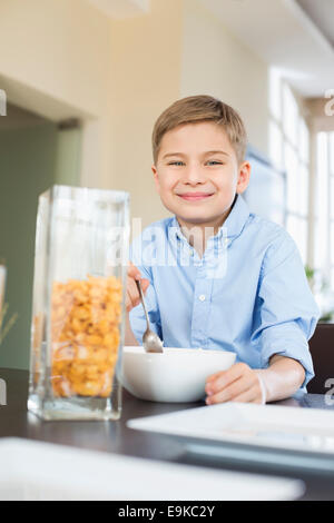 Ritratto di ragazzo sorridente versando i fiocchi di mais in un recipiente a casa Foto Stock