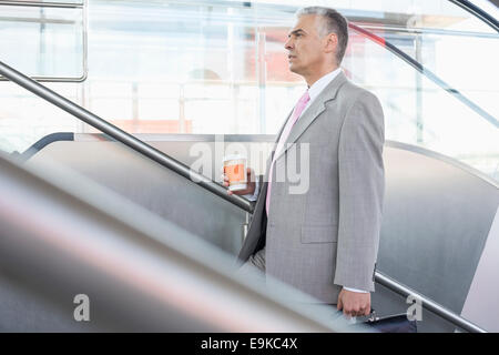 Vista laterale di mezza età imprenditore con tazza di caffè salendo le scale nella stazione ferroviaria Foto Stock