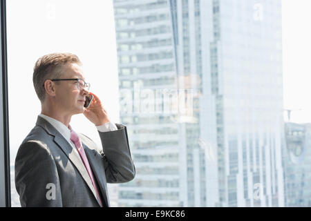 Imprenditore maturo parlando al cellulare dalla finestra Foto Stock