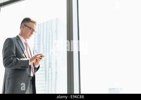 Imprenditore maturo tramite telefono cellulare dalla finestra Foto Stock