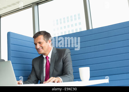 Sorridente imprenditore maturo utilizzando laptop alla scrivania Foto Stock