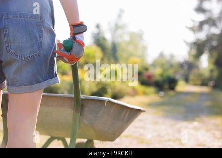 Sezione mediana vista posteriore del giardiniere femmina carriola spinta al vivaio Foto Stock