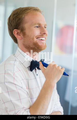Happy businessman guardando lontano tenendo pennarello presso il creative office Foto Stock