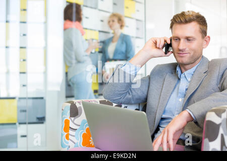 Imprenditore utilizzando tecnologie con i colleghi per discutere in background in ufficio creativo Foto Stock