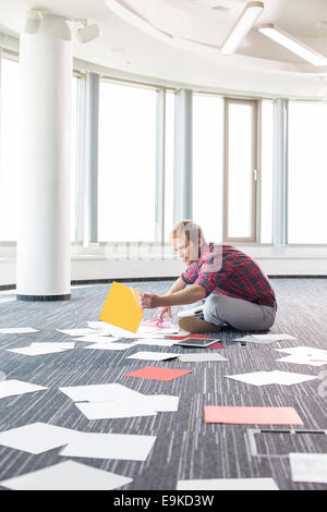 Imprenditore organizzare fotografie mentre è seduto sul pavimento presso il creative office Foto Stock