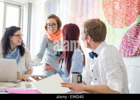 Imprenditrice dando il caffè ai colleghi in ufficio creativo Foto Stock