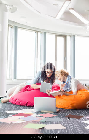 Imprenditrici utilizzando tablet PC mentre vi rilassate sulle sedie beanbag presso il creative office Foto Stock