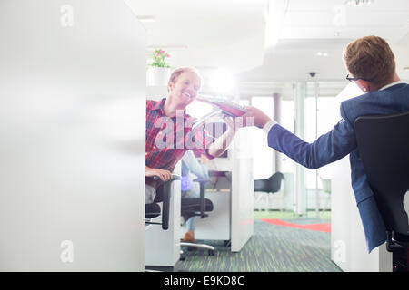 Vista posteriore di imprenditore dando i file a un collega in ufficio creativo Foto Stock