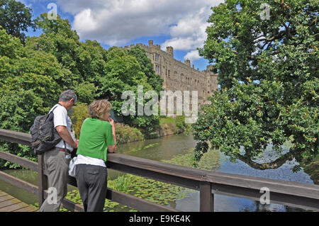 Una coppia di mezza età la visualizzazione di parte del Castello di Warwick da un ponte in legno sul fiume Avon, Inghilterra, Regno Unito. Foto Stock