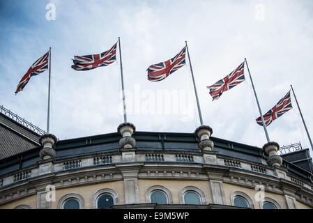 Union Jack Flags Charing Cross Londra // LONDRA, Regno Unito — Una fila di bandiere britanniche, note anche come Union Jacks, battono nella brezza in cima a un edificio di Charing Cross, direttamente di fronte a Trafalgar Square nel centro di Londra. Le distintive bandiere rosse, bianche e blu rappresentano il Regno Unito, combinando le croci di St. George (Inghilterra), St. Andrew (Scozia) e St. Patrick (Irlanda). Questa mostra patriottica si trova in una delle aree più storiche di Londra, dove Charing Cross è stato il punto di riferimento tradizionale della città fin dal XIII secolo. Le bandiere sono posizionate in un ballo Foto Stock