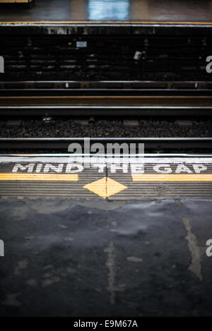 LONDRA, Regno Unito - segnali dipinti su una piattaforma della metropolitana di Londra avvertono i passeggeri di "Mind the Gap" tra il treno e la piattaforma quando salgono e scendono dal treno. Questa frase iconica è visibile in tutto il sistema della metropolitana di Londra, garantendo la sicurezza dei trasporti pubblici in tutta la città. Foto Stock