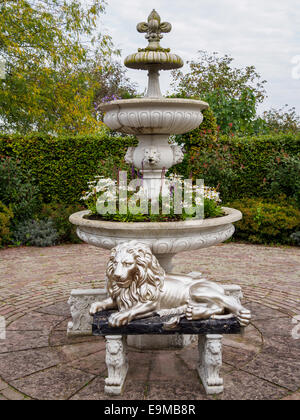 Statua di leone sdraiato fieri davanti ad una fontana floreali Foto Stock
