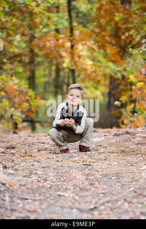 Giovane ragazzo accovacciato sul percorso del bosco in autunno Foto Stock