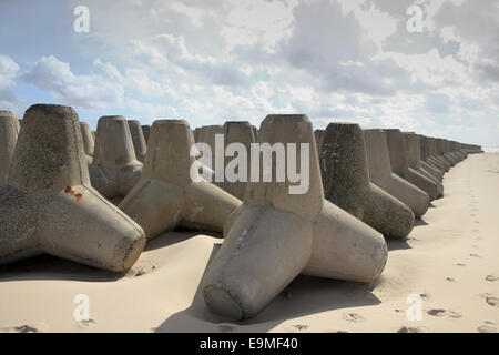 Rocce Tetrapod disposti sulla spiaggia sabbiosa contro il cielo nuvoloso Foto Stock