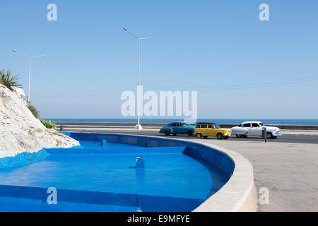 Classic Cars muovendo dalla fontana blu contro il cielo chiaro Foto Stock