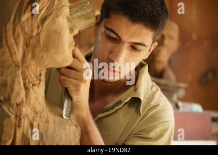 L'uomo, persone, processo giovane studente al lavoro artigiano di apprendimento della professione in classe d'arte, lavorando con la statua in legno e legno carving Foto Stock