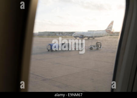 Vista da una finestra di aereo o treno di bagagli, carrelli portabagagli e piano su asfalto Foto Stock