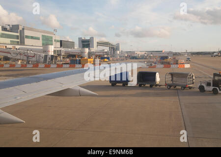 Vista da un aereo della finestra all'Aeroporto Gatwick di Londra. Piano ala, aeroporto di edifici, asfalto e treno bagaglio, bagaglio. Foto Stock