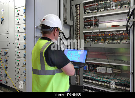 Un edificio services engineer monitora le attrezzature in un armadio elettrico nella camera di piante di un grande blocco di ufficio Foto Stock