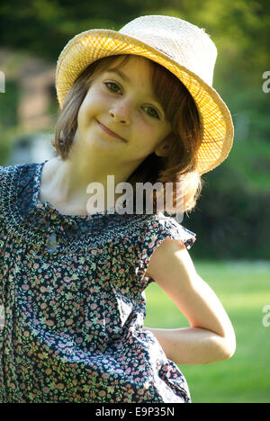 Una giovane ragazza sorridente, indossando un cappello di paglia, in un giardino soleggiato in Normandia, Francia Foto Stock