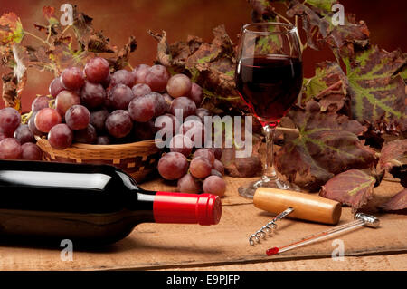 Un vecchio tavolo con una bottiglia di vino, foglie di vite e uva rossa Foto Stock