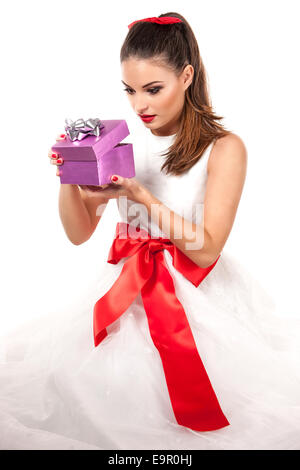 Ritratto di una giovane donna attraente in abito bianco marrone con capelli lunghi tenendo un viola scatola di Natale chiedendo circa il dono Foto Stock