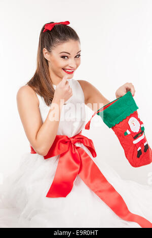 Ritratto di una giovane donna attraente in abito bianco pieno di emozioni alla ricerca di regali in calza di Natale Foto Stock