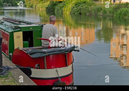 L'uomo la pesca dal retro di un narrowboat, fiume Nene, Northampton REGNO UNITO Foto Stock