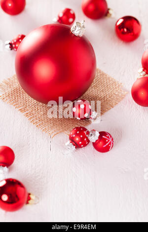 Rosso di Natale a tema sfondo con una grande pallina su di una piazza di rustico hessian circondato da decorativi sfere di piccole dimensioni con polk Foto Stock