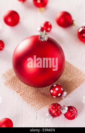 Rosso di Natale a tema sfondo con una grande pallina su di una piazza di rustico hessian circondato da decorativi sfere di piccole dimensioni con polk Foto Stock