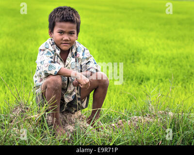 Un misterioso ragazzo cambogiano in posa per un ritratto seduto su un campo di riso vicino a Siem Reap, Cambogia. Foto Stock