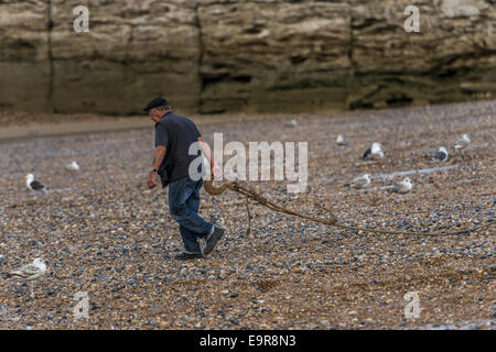 Un lavoratore contribuisce a lanciare la flotta costiera di barche da pesca dalla spiaggia di Stade in Hastings Foto Stock