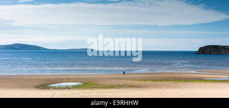 La figura di Lone, un pescatore, passeggiava lungo la remota spiaggia di sabbia di Gruinard sotto il cielo ceruleo nella costa occidentale DELLA SCOZIA Foto Stock