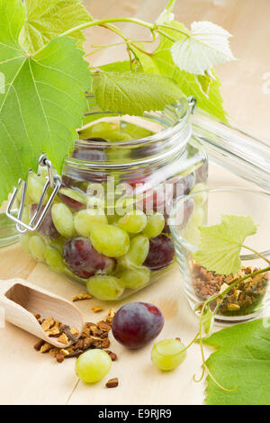 Vaso di vetro con le conserve di uve, mosto di foglie e spice sul tavolo di legno Foto Stock