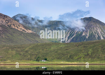 Di piccole dimensioni e di colore bianco crofters solitario cottage immerso sotto la gamma della montagna si riflette nelle acque del loch sull isola di Skye nel Highl Foto Stock