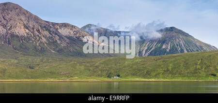 Di piccole dimensioni e di colore bianco crofters solitario cottage immerso sotto la gamma della montagna si riflette nelle acque del loch sull isola di Skye nel Highl Foto Stock