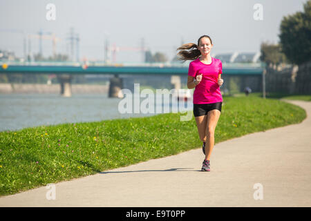 Giovane carina ragazza pareggiatore corre sulla via lungo il fiume nella citta'. Foto Stock