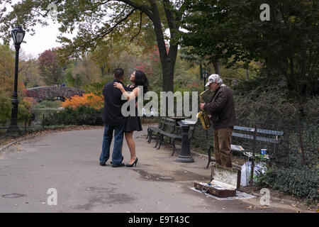 Un giovane a ballare la musica da un uomo suonare il sassofono nel Central Park di New York City. Foto Stock