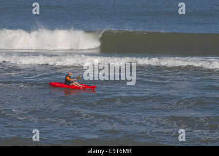 Cape Hatteras, Outer Banks, North Carolina, Stati Uniti d'America - 17 ottobre 2013: Un uomo su un kayak rosso brillante pagaia lungo le onde del mare Foto Stock