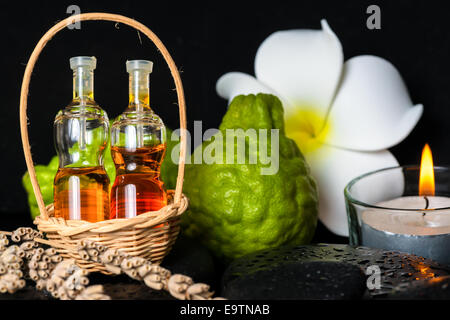 Centro termale aromatico concetto di bottiglie di olio essenziale nel cestello, fiore, bergamotto, candele e nero zen pietre di basalto di rugiada Foto Stock