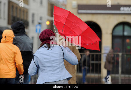 Una donna lotte con il suo rosso "Mantenere la calma e a portare sul' ombrello lungo Brighton Seafront durante le tempeste Foto Stock