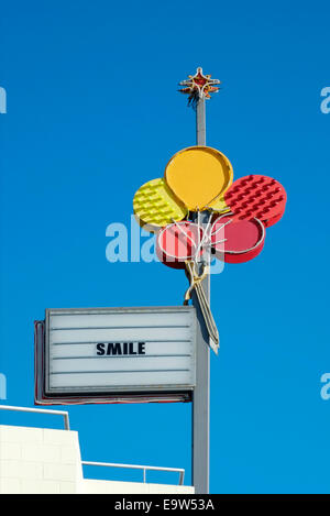 Luci al neon colorate segno raffigurante il rosso e il giallo di palloncini con la parola sorriso contro un profondo cielo blu England Regno Unito Foto Stock