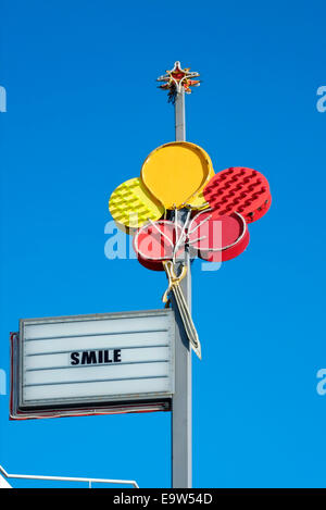 Luci al neon colorate segno raffigurante il rosso e il giallo di palloncini con la parola sorriso contro un profondo cielo blu England Regno Unito Foto Stock