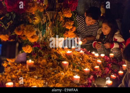 I bambini accendono le candele sulla tomba di un membro della famiglia a San Felipe del Agua cimitero durante il Giorno dei Morti Festival noto in spagnolo come d'un de Muertos il 2 novembre 2014 a Oaxaca, Messico. Foto Stock