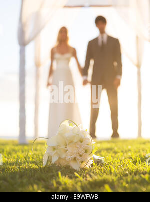 Nozze, bella sposa e lo Sposo tenendo le mani. La messa a fuoco del bouquet, profondità di campo Foto Stock