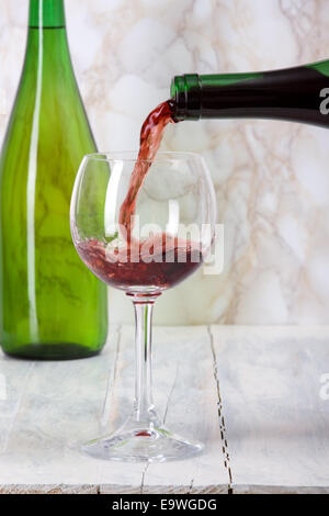 Il vino rosso è versata da una bottiglia in un bicchiere. Foto Stock