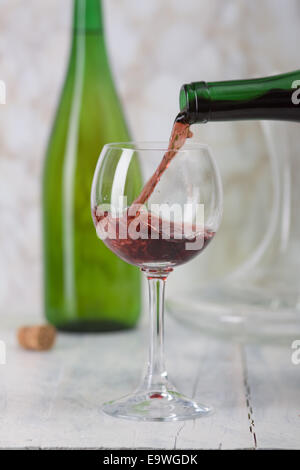 Il vino rosso è versata da una bottiglia in un bicchiere. Foto Stock