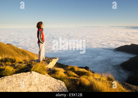 Escursionista femmina di raggiungere il suo obiettivo alla cima della montagna e guardando il maestoso panorama italiano della Alpi occidentali con il cloud Foto Stock